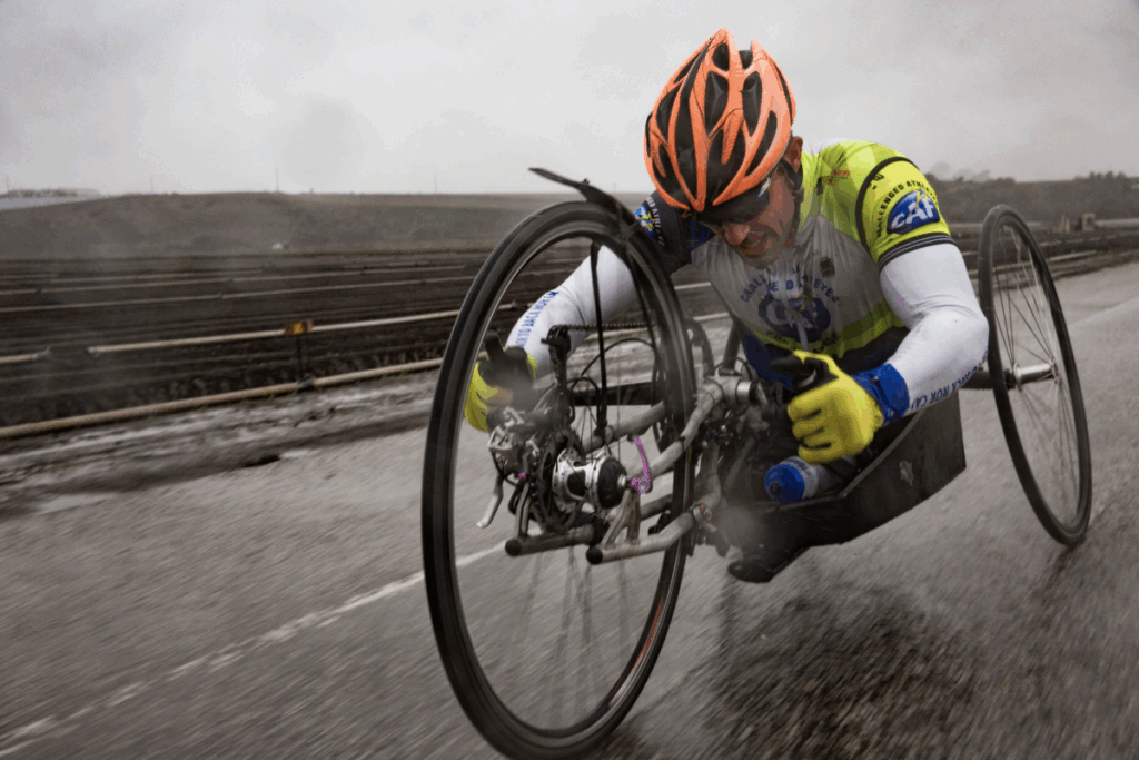 Andre Kajlich racing in a handcycle on a rainy road, wearing an orange helmet and CAF cycling gear.