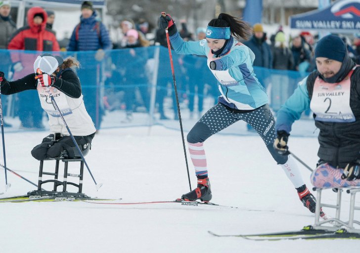 Adaptive skiers compete in a cross-country race at Sun Valley, pushing forward with poles on a packed snow track.