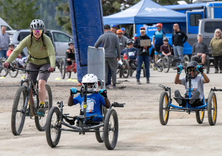 Two children riding adaptive mountain bikes with an adult cycling nearby.