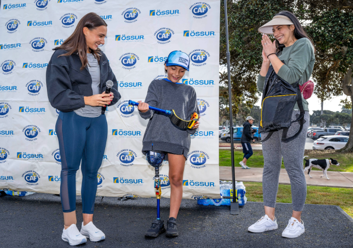 Youth athlete Estella Madrigalreceiving a prosthetic leg grant on stage at an ossur running and mobility clinic on stage smiling