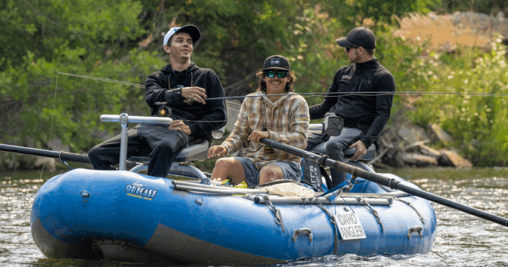 Three participants smiling and fishing from a blue raft on the river at CAF Idaho Water Sports Weekend