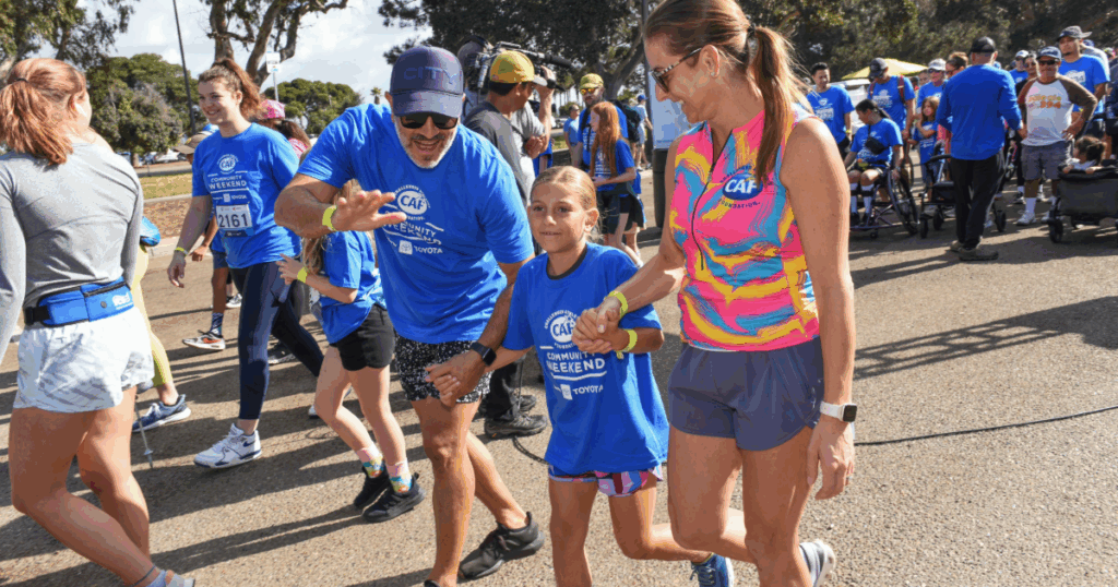 A participant in a bright multicolor CAF tank top walks hand in hand with a young girl, joined by other walkers at the event.