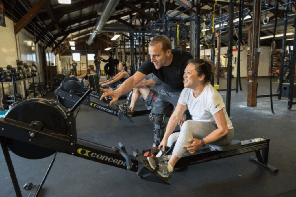 Adaptive CrossFit coach, Max Conserva, guiding an athlete on a rowing machine inside the gym.
