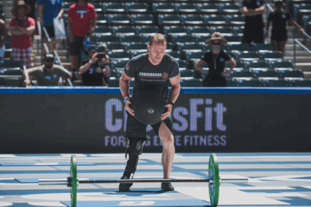 Athlete with a prosthetic leg lifting an Atlas stone during a CrossFit competition.