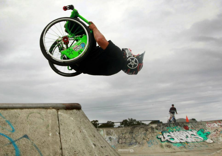 Aaron Fotheringham performs a backflip in a wheelchair at a skatepark, showcasing adaptive freestyle skills.