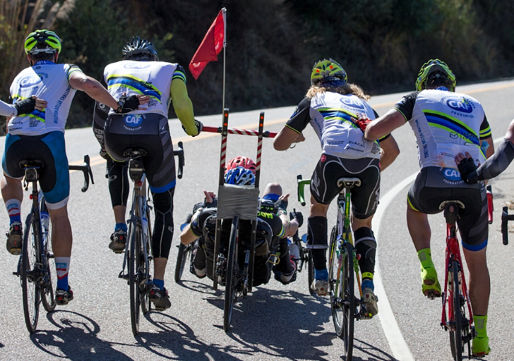 Group of cyclists supporting a handcyclist up a hill during a team ride.
