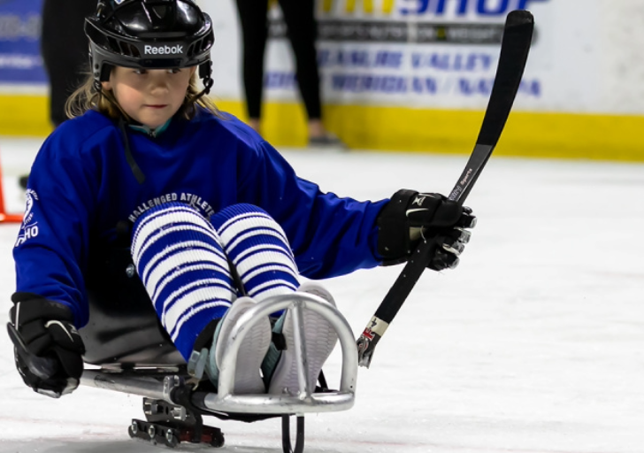 Young athlete playing sled hockey on the ice during a practice session, focused while pushing forward with her stick.