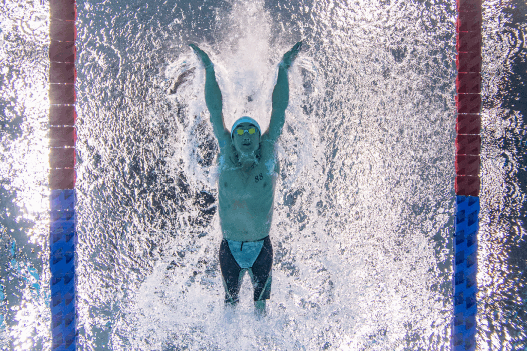 Paralympic swimmer captured underwater pushing off the wall in a backstroke start, with splashes on both sides of the lane.