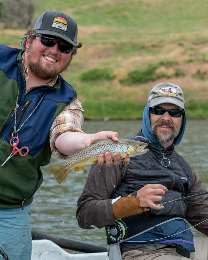 Two people holding a fish on a boat by a river.