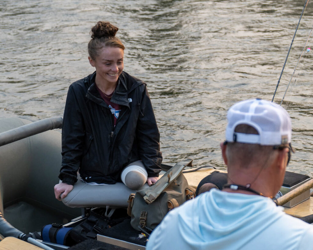 Two people on a rubber raft on a river, including one smiling individual with a lower limb difference.