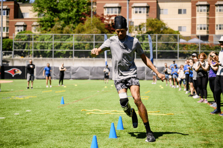 Athlete with a running blade practices agility drills on a grass field, weaving through blue cones during a CAF and Össur running and mobility clinic.