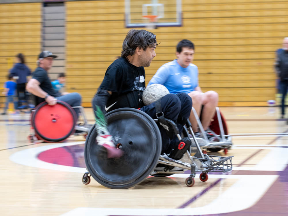 Wheelchair rugby game in a gymnasium with players in motion.