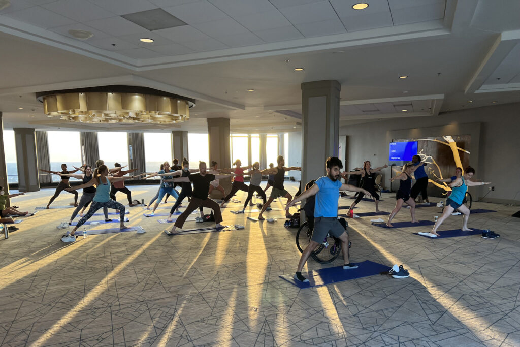 Athletes of all abilities practicing yoga together in a large, sunlit room.
