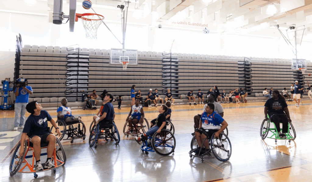 Group of youth athletes in sport wheelchairs play basketball, all looking up toward the hoop during a game.