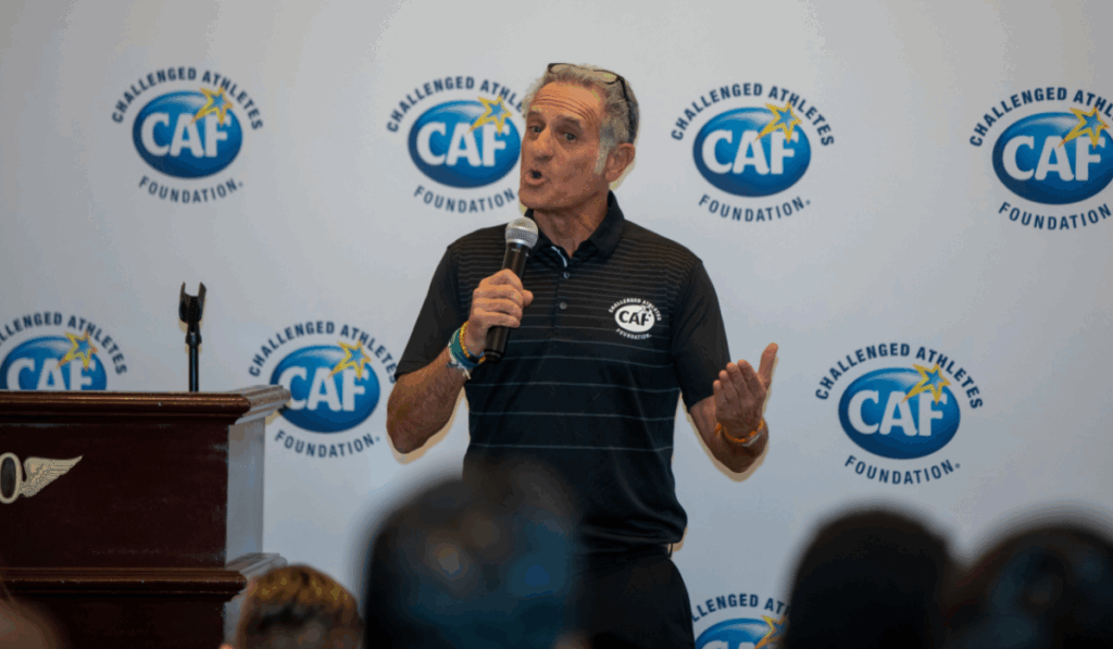 CAF co-founder Bob Babbitt speaks at a podium with a microphone, standing in front of a backdrop with the CAF logo