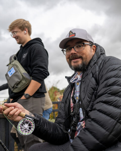 Two men outdoors, one holding a fishing rod with a colorful reel.