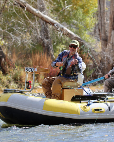 Person fly fishing from a yellow and white inflatable raft on a river.
