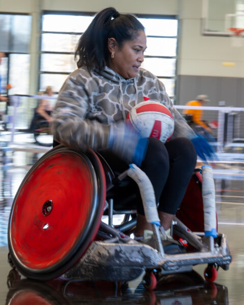 Person in a sports wheelchair holding a volleyball on a basketball court.