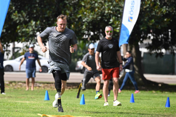 Athletes participate in an outdoor training drill on grass, running between blue cones while coaches and other participants observe.