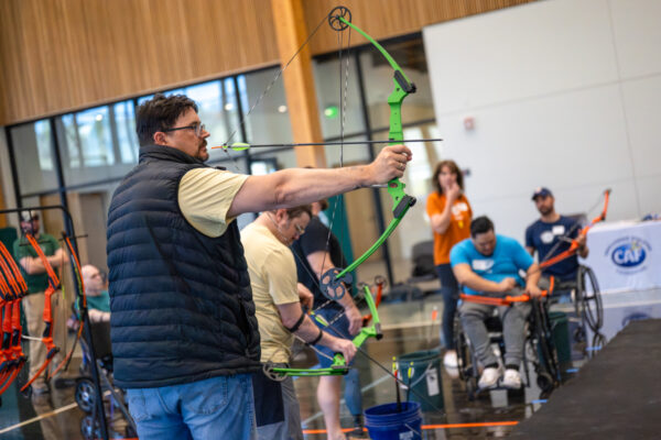 People participating in an indoor archery activity, with some individuals in wheelchairs.