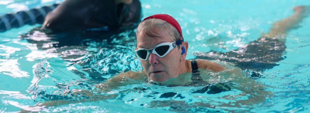 A woman swimming in an indoor pool. Another person is directly behind her.