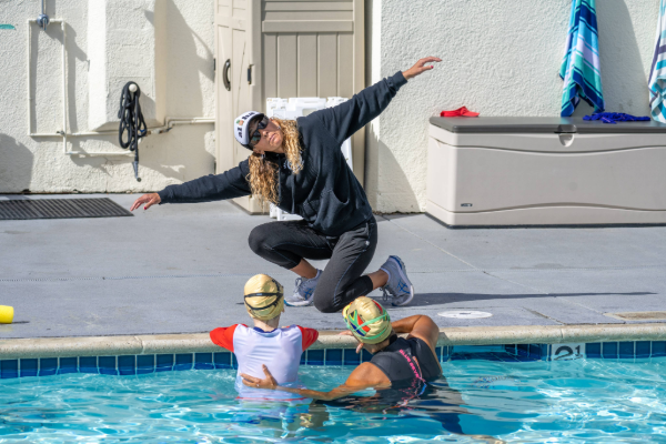 Instructor standing in the water guiding a swimmer during a drill near the pool wall with splashing water in a lap lane.